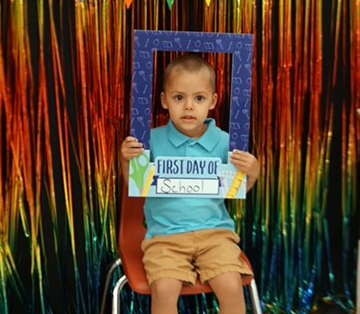School boy sitting on chair holding up first day of school frame